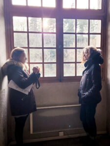 Manon C en cours de préparation d'une visite guidée avec une médiatrice culturelle, devant une grande fenêtre. Le visage de la médiatrice est flouté.